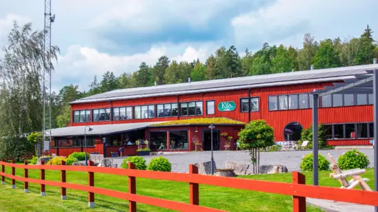Kila Möblers butik i Kiladalen. En stor faluröd byggnad med parkering på framsidan omgiven av grön natur.